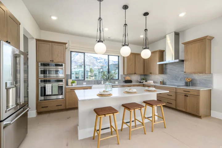 Gourmet kitchen featuring a large central island with seating, stainless steel appliances, wood-finish cabinetry, a striking stone backsplash, and recessed lighting