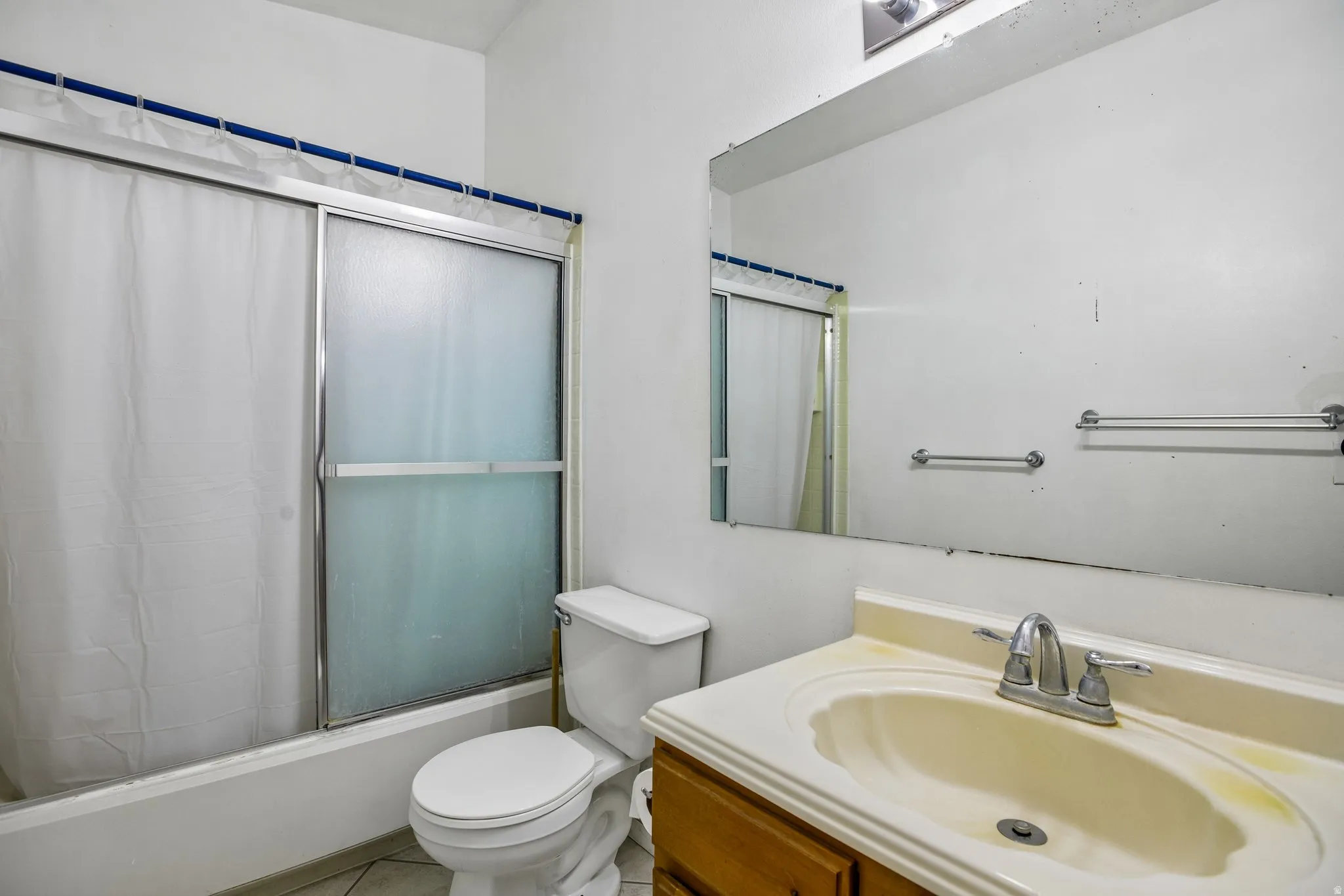 Bathroom featuring a vanity with an integrated sink, a large wall-mounted mirror, a toilet, and a shower-tub combination with sliding glass doors