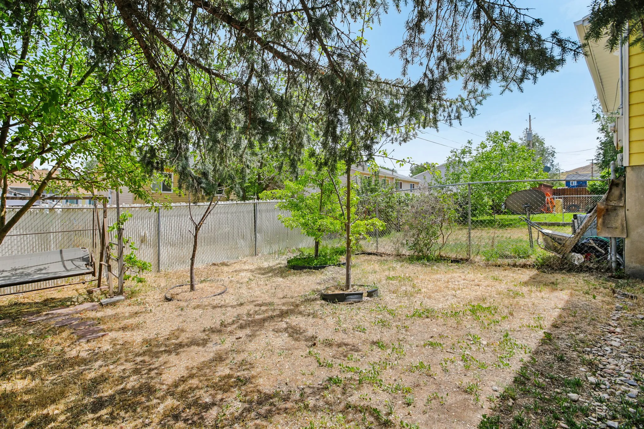 Fully fenced backyard featuring mature trees, a chain-link fence with privacy slats, and ample space