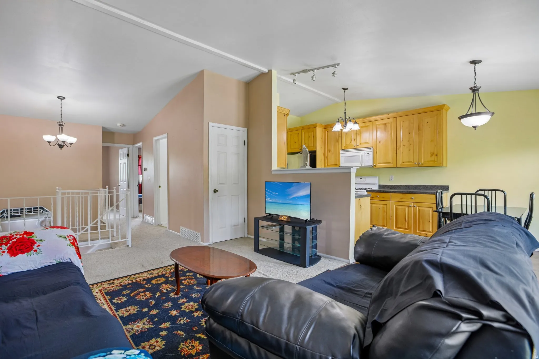 Open-concept living space featuring vaulted ceilings, a carpeted area, and light wood cabinetry in the kitchen