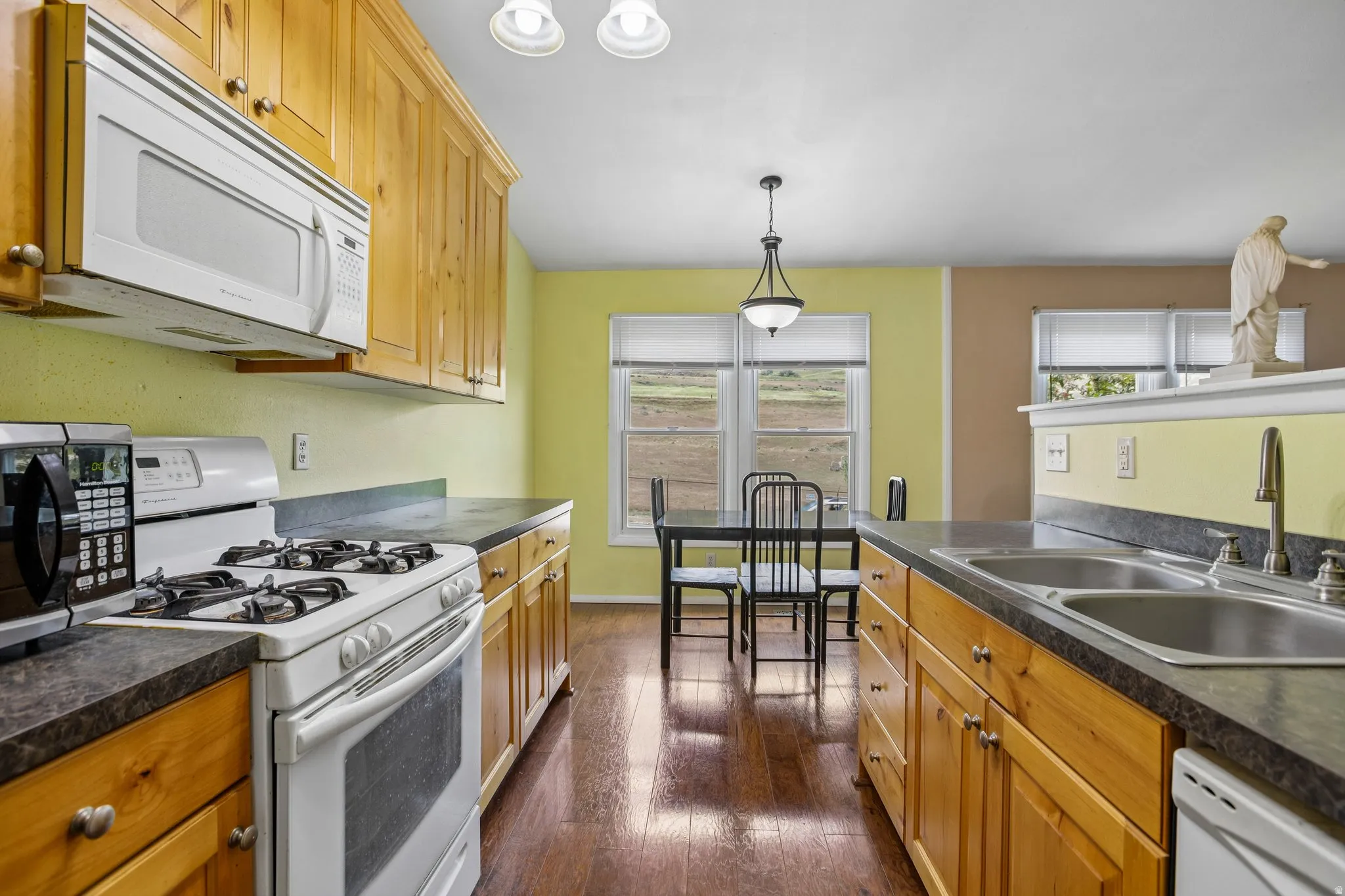 Kitchen featuring wood-finish cabinetry, dark countertops, and a full suite of appliances including a range and microwave