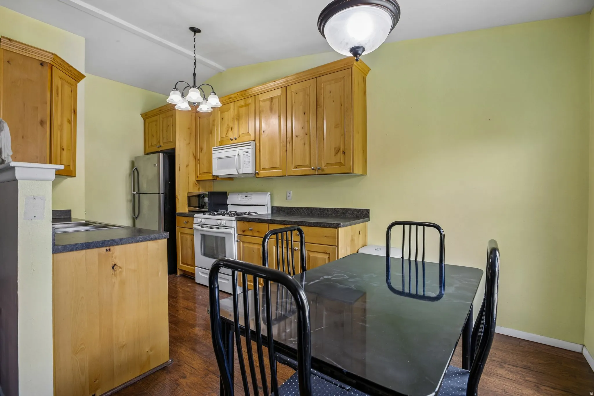 Eat-in kitchen featuring wood cabinetry, dark countertops, wood-finish flooring, and a white oven with a stainless steel refrigerator