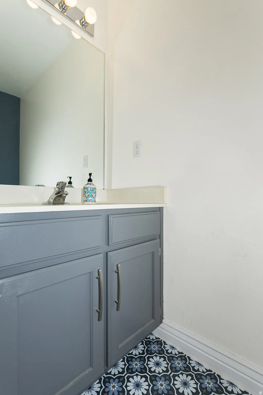 Bathroom vanity featuring grey cabinetry, white countertop, and patterned floor tiling