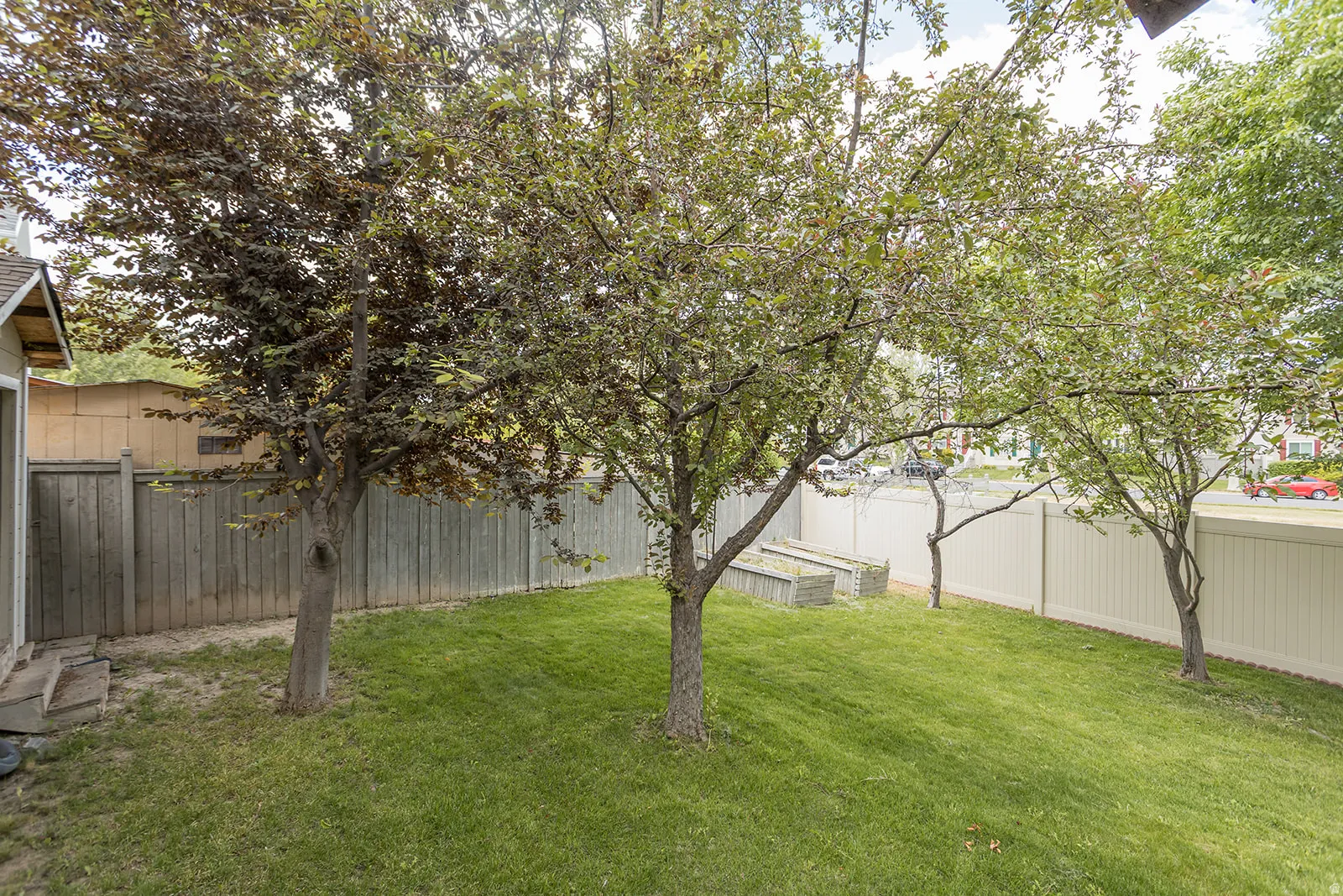 Expansive grassy yard with mature trees, bordered by a privacy fence and a white vinyl fence