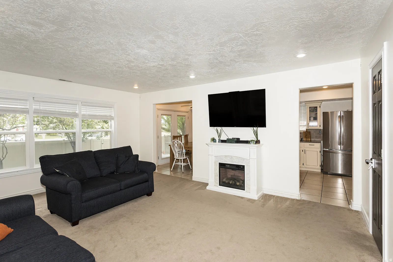 Living area featuring a white electric fireplace with a mantel, recessed lighting, and large windows with horizontal blinds