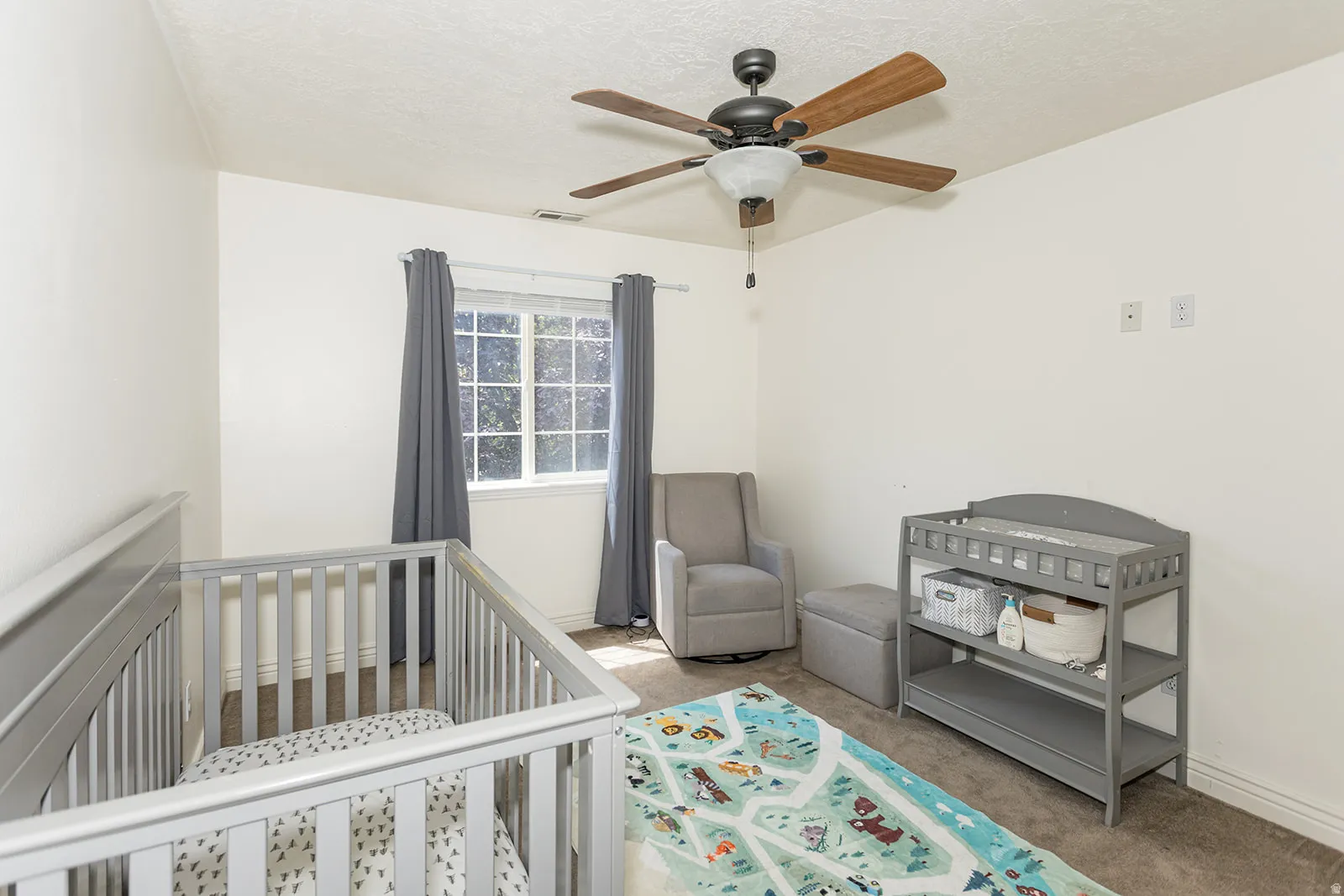 Bright interior space featuring a window with natural light, a ceiling fan with wood-finish blades, soft wall-to-wall carpeting, and neutral paint