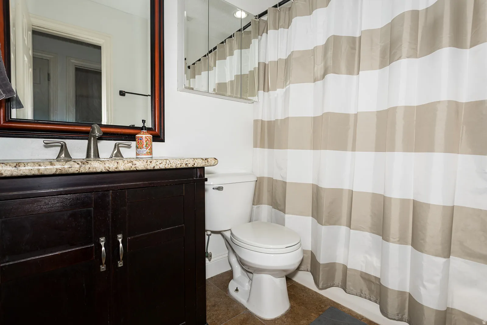 Bathroom featuring a dark wood-finish vanity with a stone countertop, an undermount sink, and a framed mirror