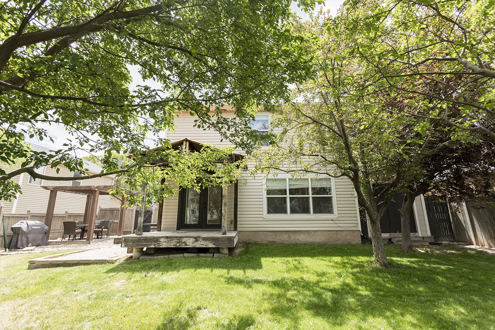 Expansive backyard featuring a manicured lawn, established trees, a wood pergola, and a patio area