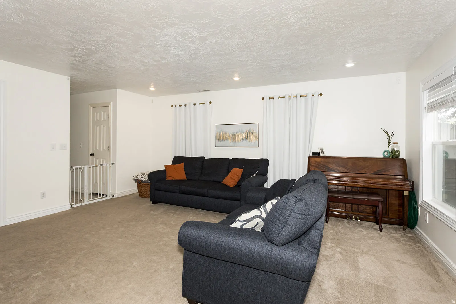 Carpeted living area featuring white walls, recessed lighting, and a prominent window with blinds