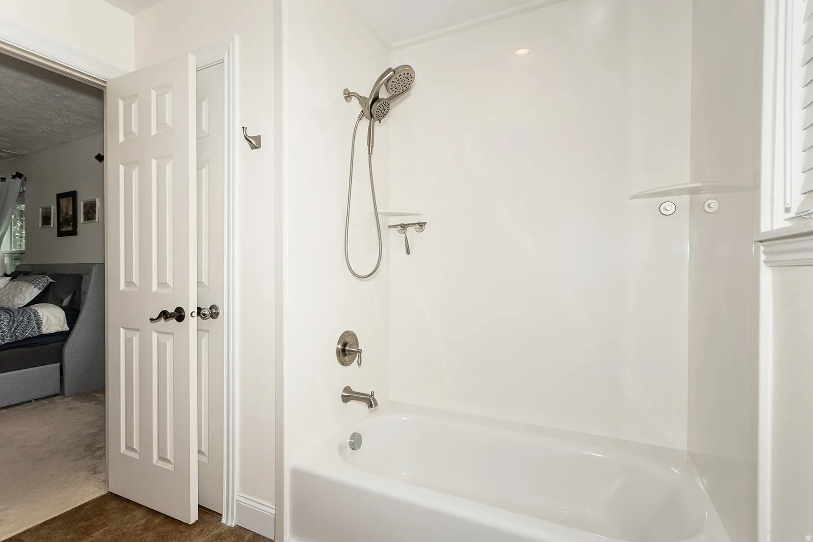 White bathtub and shower combination featuring brushed nickel fixtures, a multi-setting showerhead, and integrated shelving