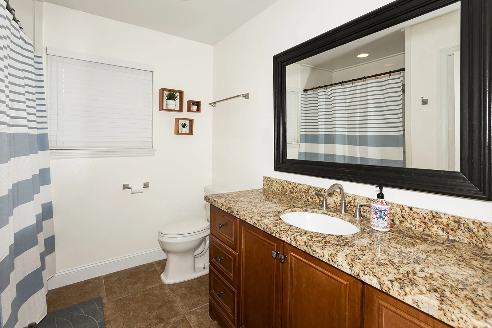 Bathroom featuring an expansive vanity with a light-colored stone countertop, an undermount sink, and wood-finish cabinetry