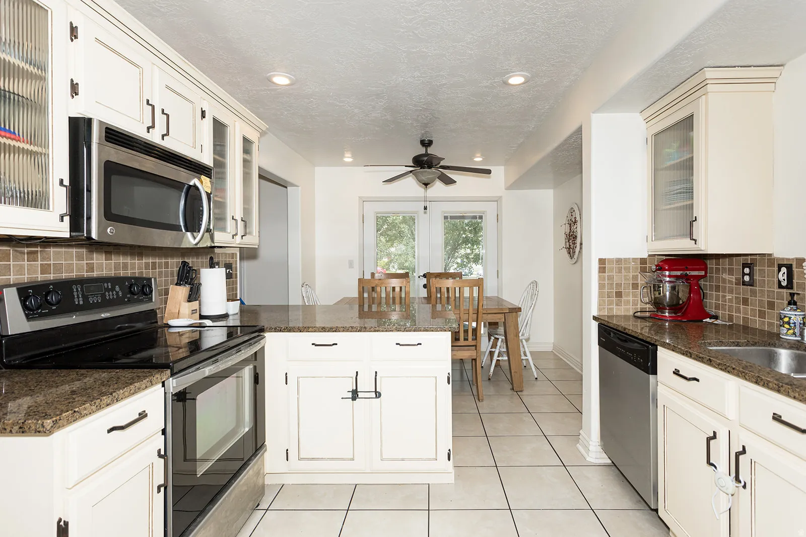 Kitchen featuring cream-colored cabinetry, granite countertops, stainless steel appliances, and a tiled backsplash