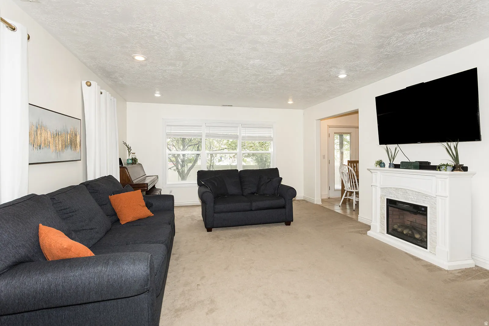 Living room featuring a white mantelpiece with a built-in fireplace, recessed lighting, and a large window with blinds