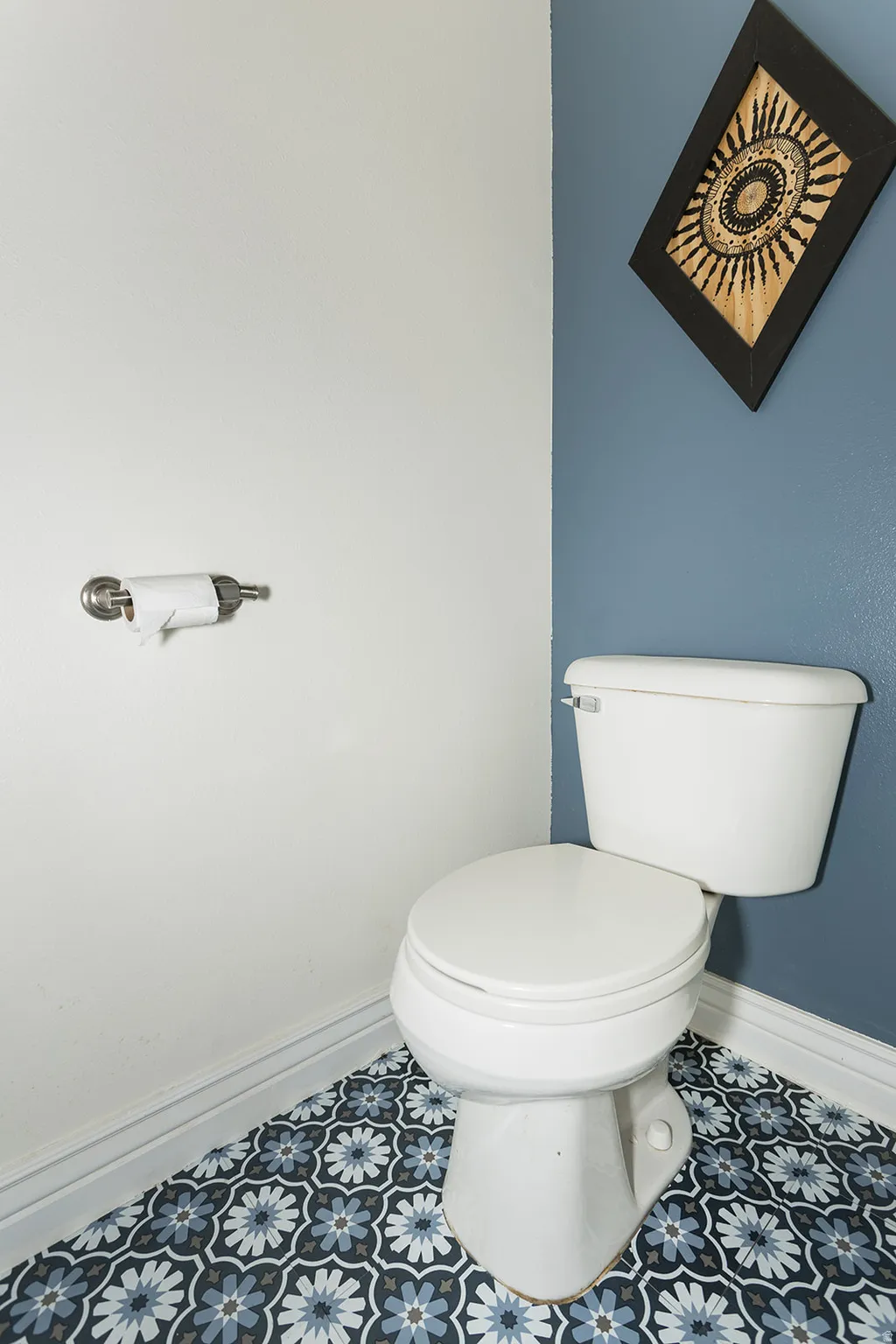 Powder room featuring a white toilet, patterned floor tiles in shades of blue and white, and a two-tone wall finish with white and blue paint