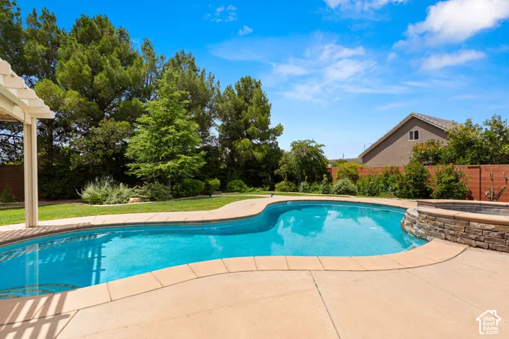 Curved swimming pool with surrounding concrete patio and an integrated stone-clad spa