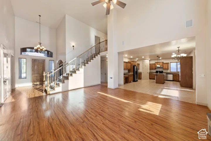 Spacious open-concept living area showcasing soaring vaulted ceilings, a floating staircase with metal railings, and warm wood-finish flooring throughout