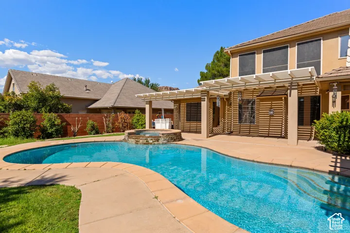 Outdoor oasis featuring a freeform swimming pool with a stone-clad spa, expansive patio, and a slatted pergola structure