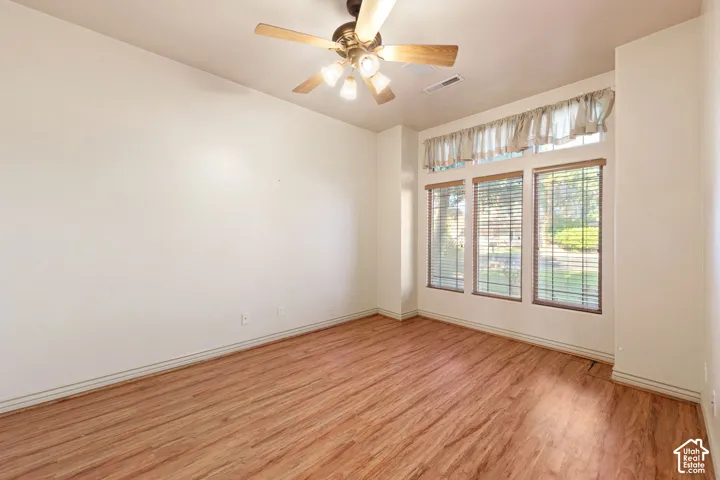 Wood-finish flooring, ceiling fan with integrated lighting, multiple windows with blinds, and white wall finishes
