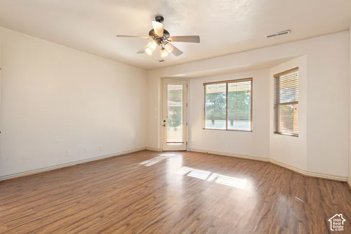 Wood-finish flooring throughout, ceiling fan with integrated lighting, bay window, and a glass-paneled door