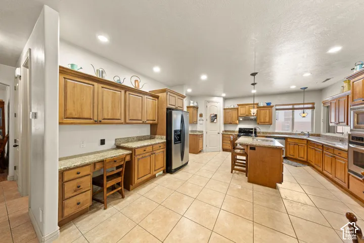 Spacious kitchen featuring light wood cabinetry, recessed lighting, stainless steel appliances, a center island with pendant lighting, and light-toned tile flooring