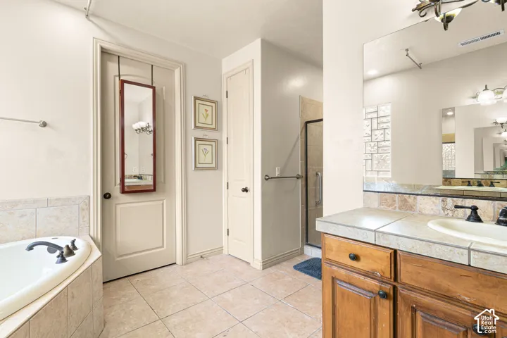 Bathroom featuring a corner soaking tub, a shower enclosure with glass block accent, and a vanity with a tile countertop and integrated sink
