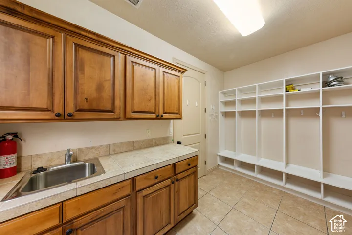 Utility room featuring a built-in sink with a tiled countertop, wood-finish cabinetry, and extensive built-in white shelving