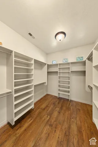 Expansive closet featuring wood-finish flooring, white shelving units, clothing rods, and recessed glass block windows