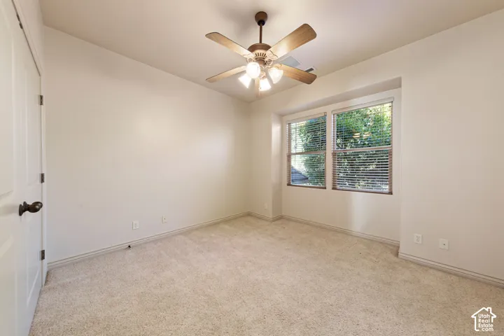 Neutral-toned carpeting, ceiling fan with integrated lighting, two windows with blinds, and a white paneled door with dark hardware