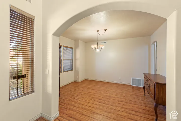 Spacious room featuring an arched entryway, wood-finish flooring, multiple windows with horizontal blinds, and a traditional ceiling light fixture