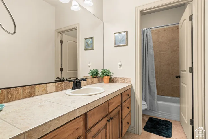 Bathroom vanity featuring a tile countertop, wood-finish cabinetry, and an integrated sink with a black faucet