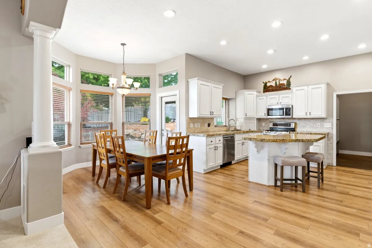 Open-concept kitchen and dining area featuring light wood-finish flooring, white cabinetry, and granite countertops