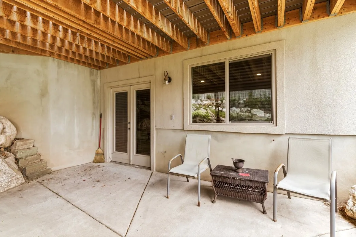 Concrete patio area featuring a textured stucco exterior, exposed wood joists, and a glass sliding door