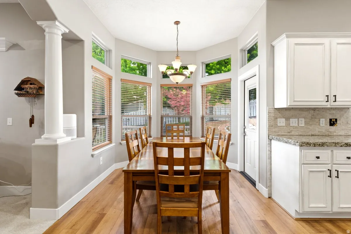 Bay window dining area with wood-finish flooring, featuring a chandelier and multiple windows with wood blinds
