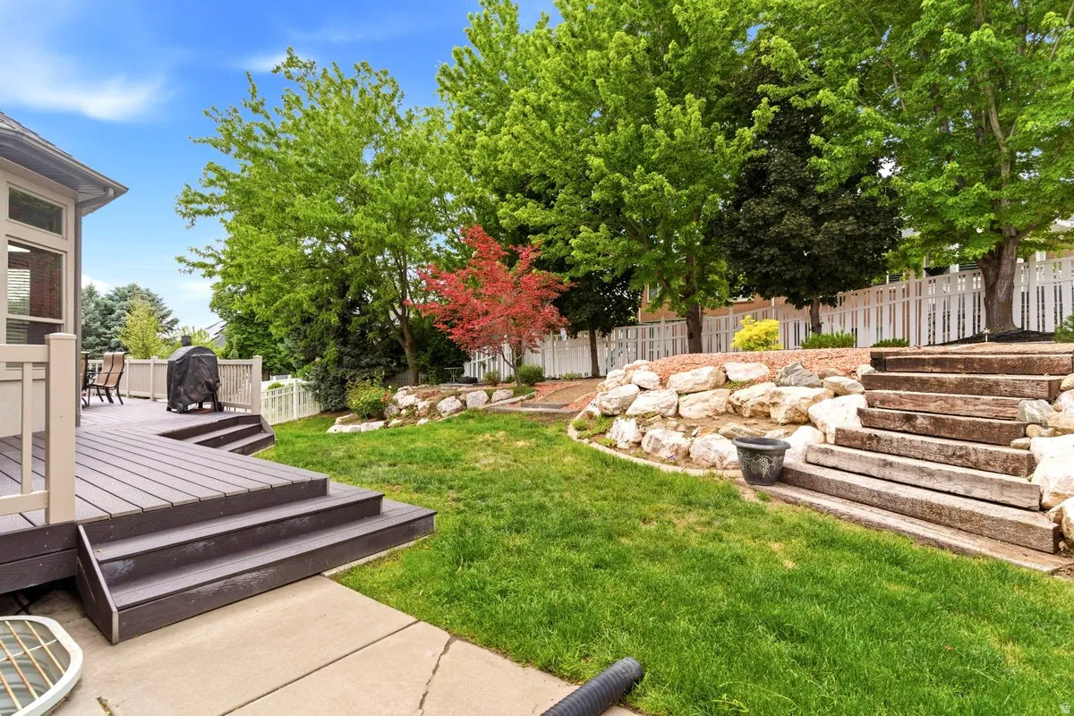 Expansive backyard featuring a composite deck with steps, a manicured lawn, and mature trees