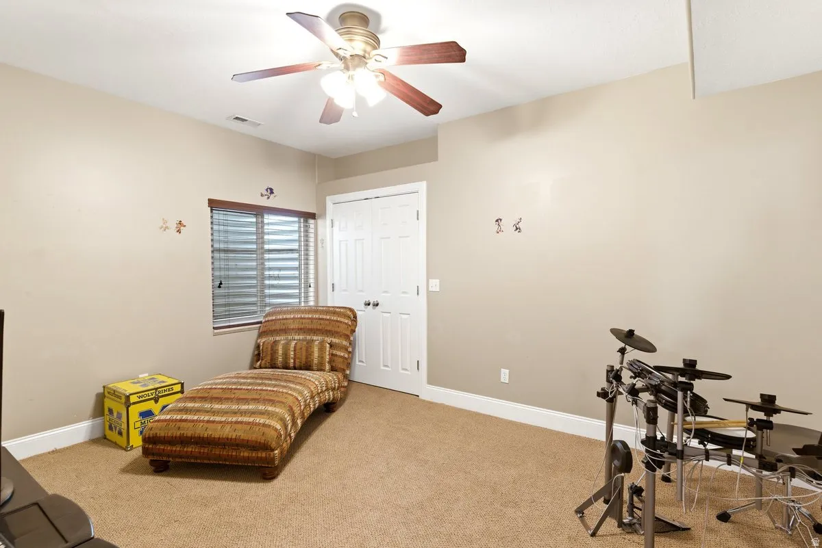 Carpeted room featuring a ceiling fan with light fixture, recessed window with blinds, white paneled door, and neutral wall tones