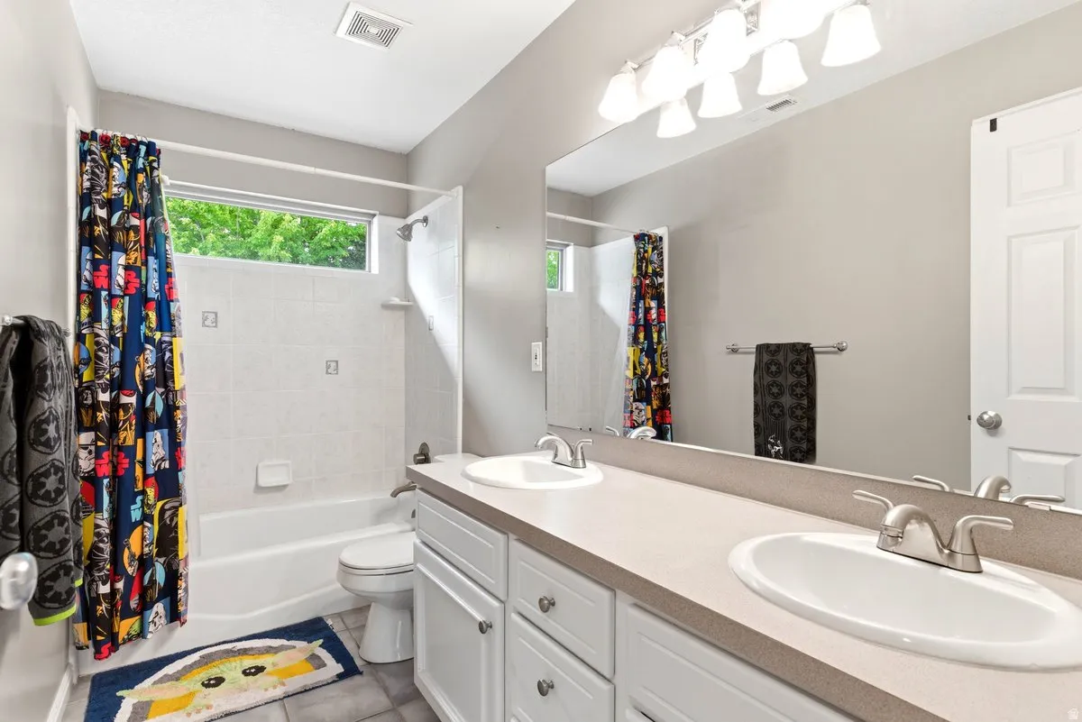 Bathroom featuring a double vanity with integrated sinks, a tub/shower combination with white tile surround, and a horizontal window providing natural illumination