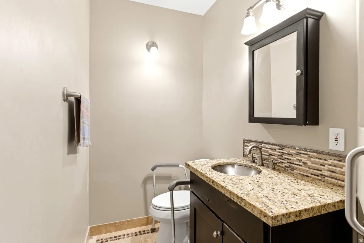Bathroom vanity featuring a granite countertop, stainless steel sink, dark wood cabinetry, and a mosaic tile backsplash