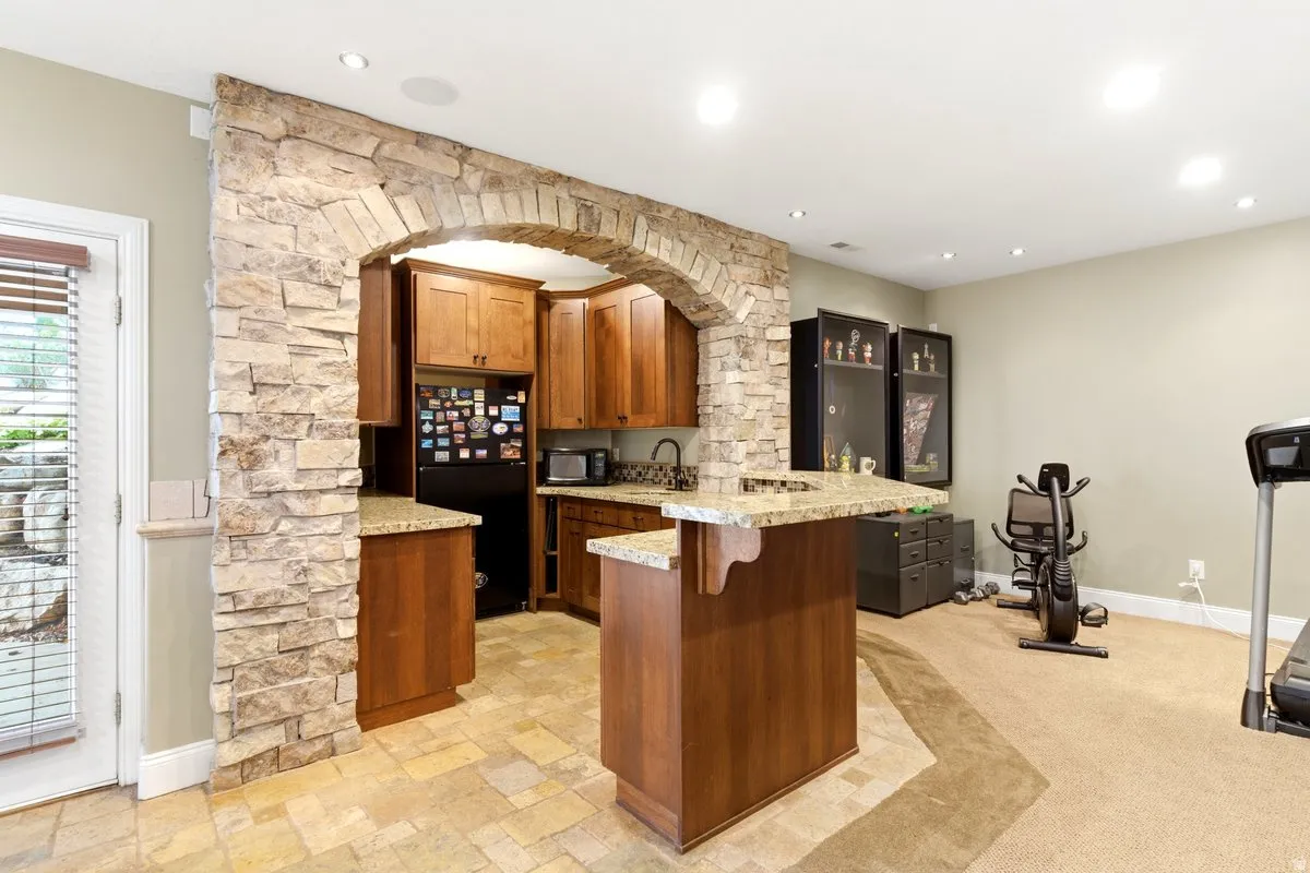 Stone archway defining a kitchen area featuring wood cabinetry, granite countertops, and tile flooring