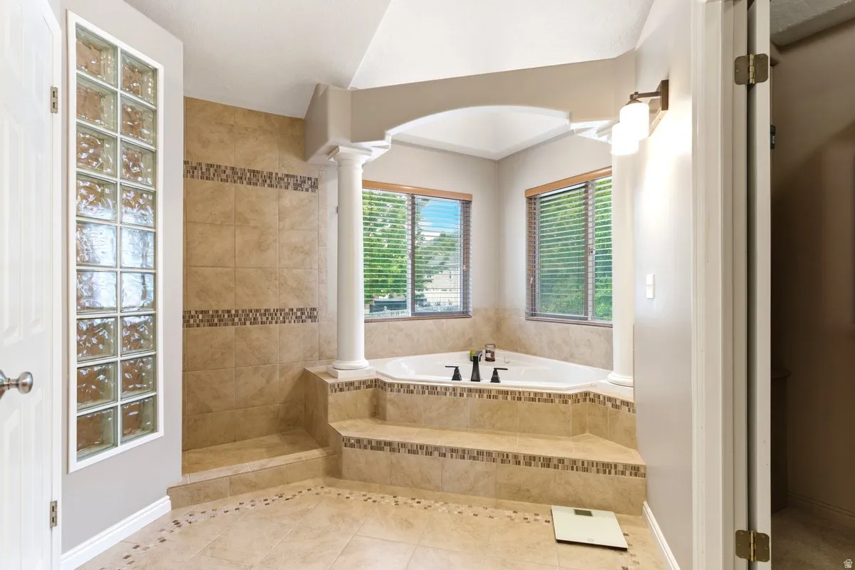 Spacious bathroom featuring a corner soaking tub, tiled shower with glass block wall, and decorative column accents