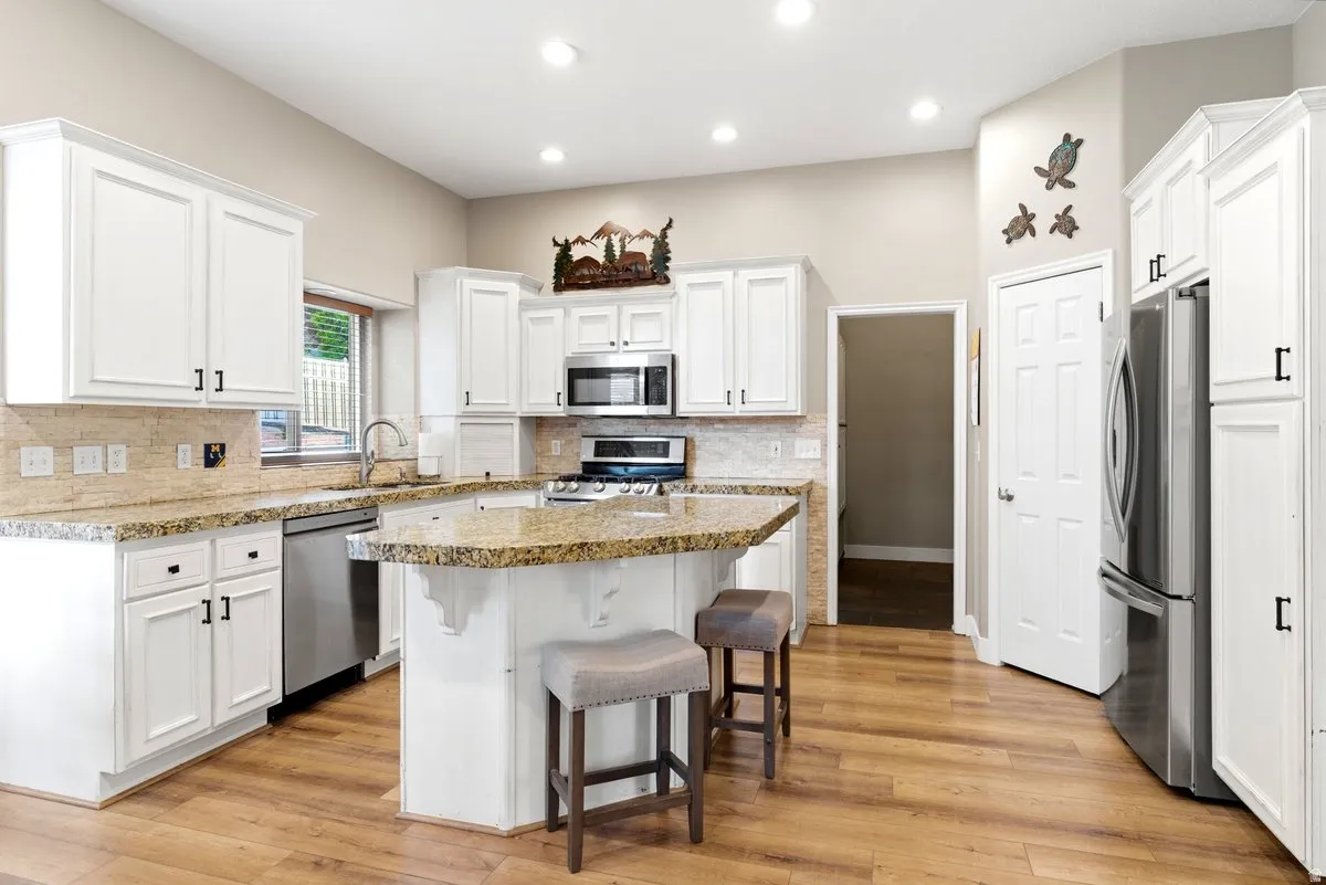Kitchen featuring white cabinetry, granite countertops, stainless steel appliances, a breakfast bar, and wood-finish flooring