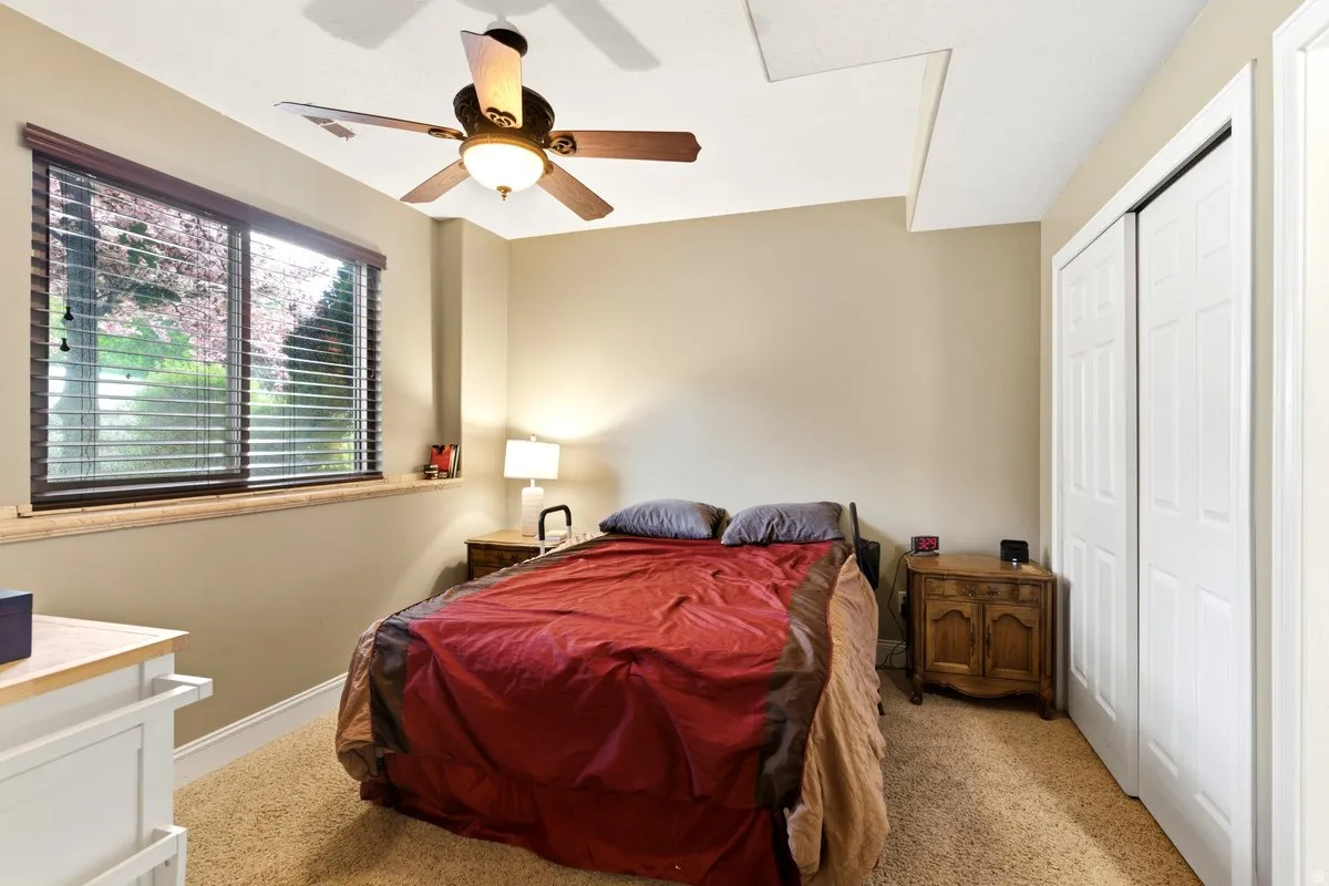 Inviting room featuring a large window with horizontal blinds, a ceiling fan with integrated lighting, textured carpeting, and white bi-fold closet doors