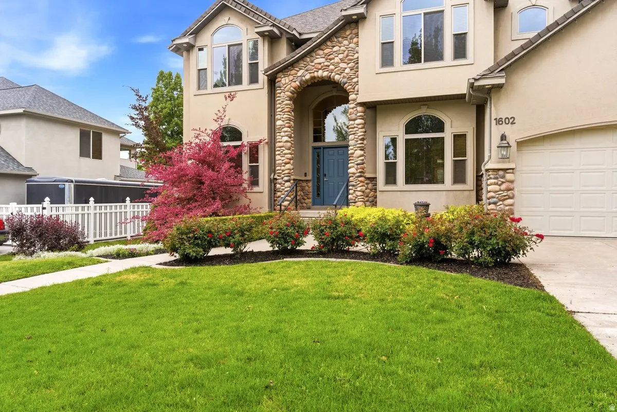 Stucco and stone facade featuring an arched entry, prominent windows, a two-car garage, and manicured landscaping