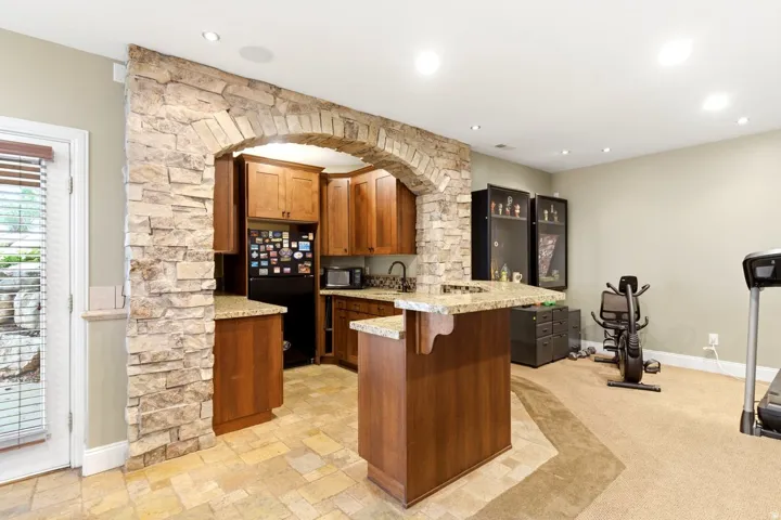 Stone archway defining a kitchen area featuring wood cabinetry, granite countertops, and tile flooring