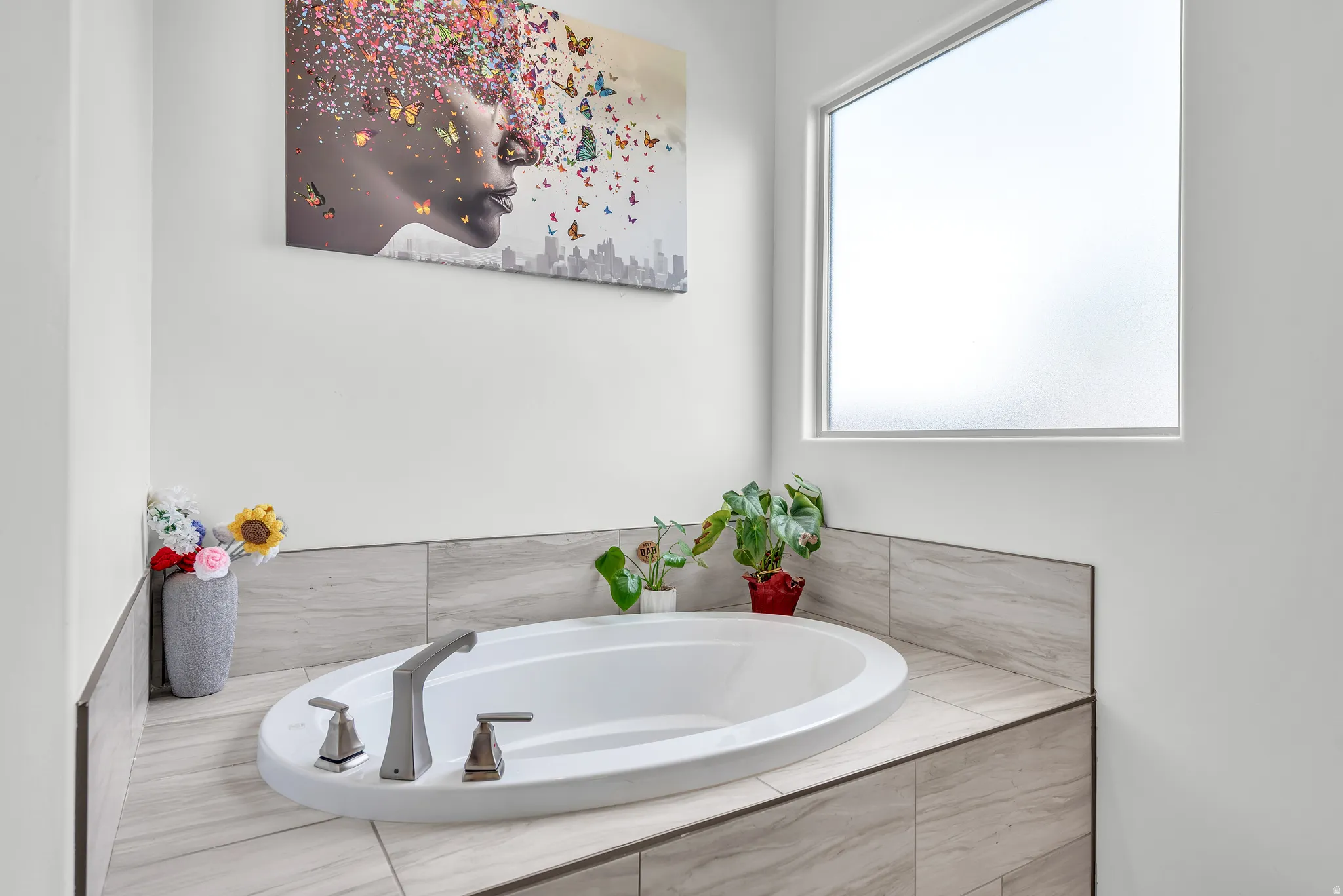 Oval soaking tub with deck-mounted brushed nickel fixtures, set into a tiled surround featuring light-toned large format tiles