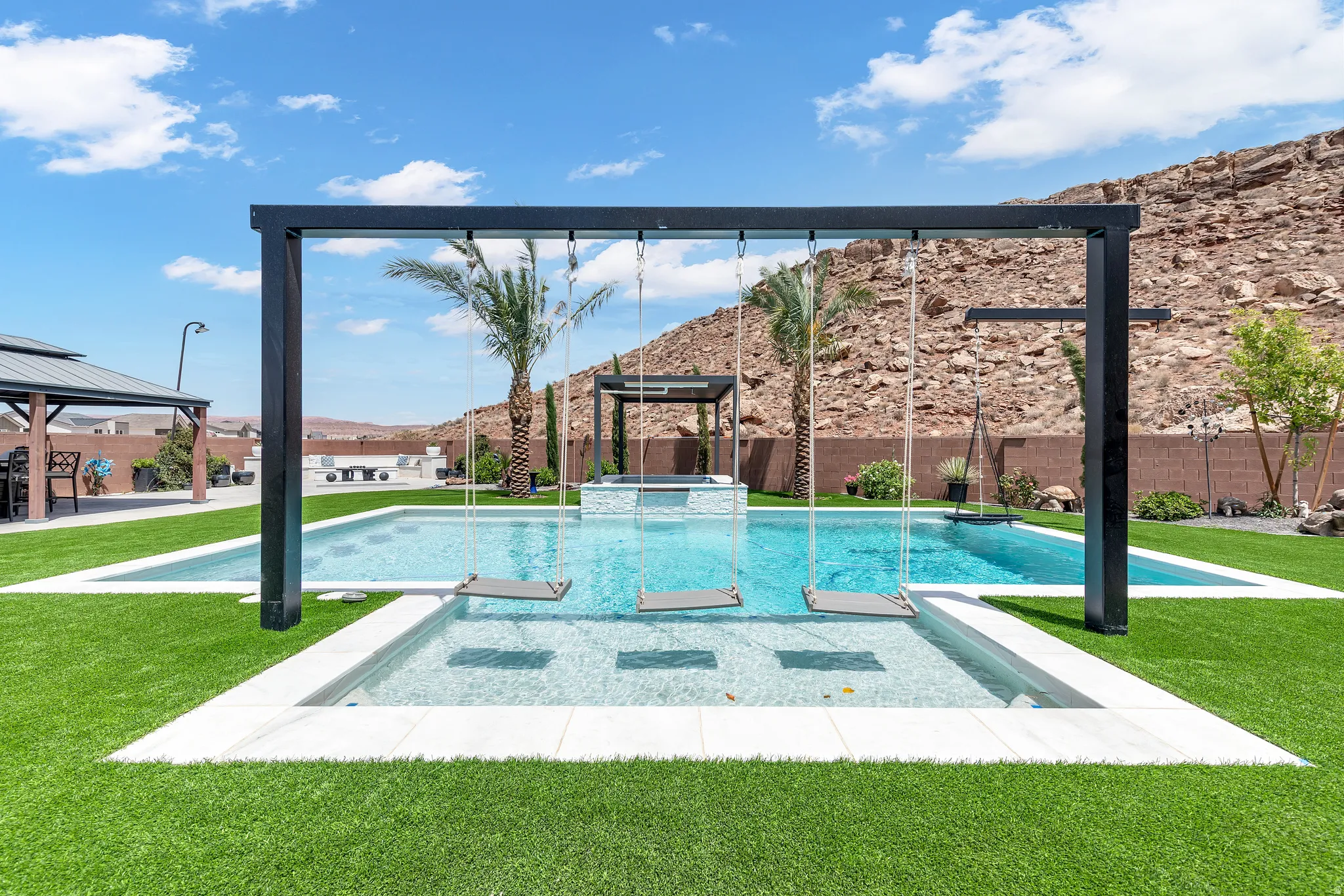 Resort-style pool area featuring a tanning ledge with built-in swings, artificial turf landscaping, and a separate elevated spa