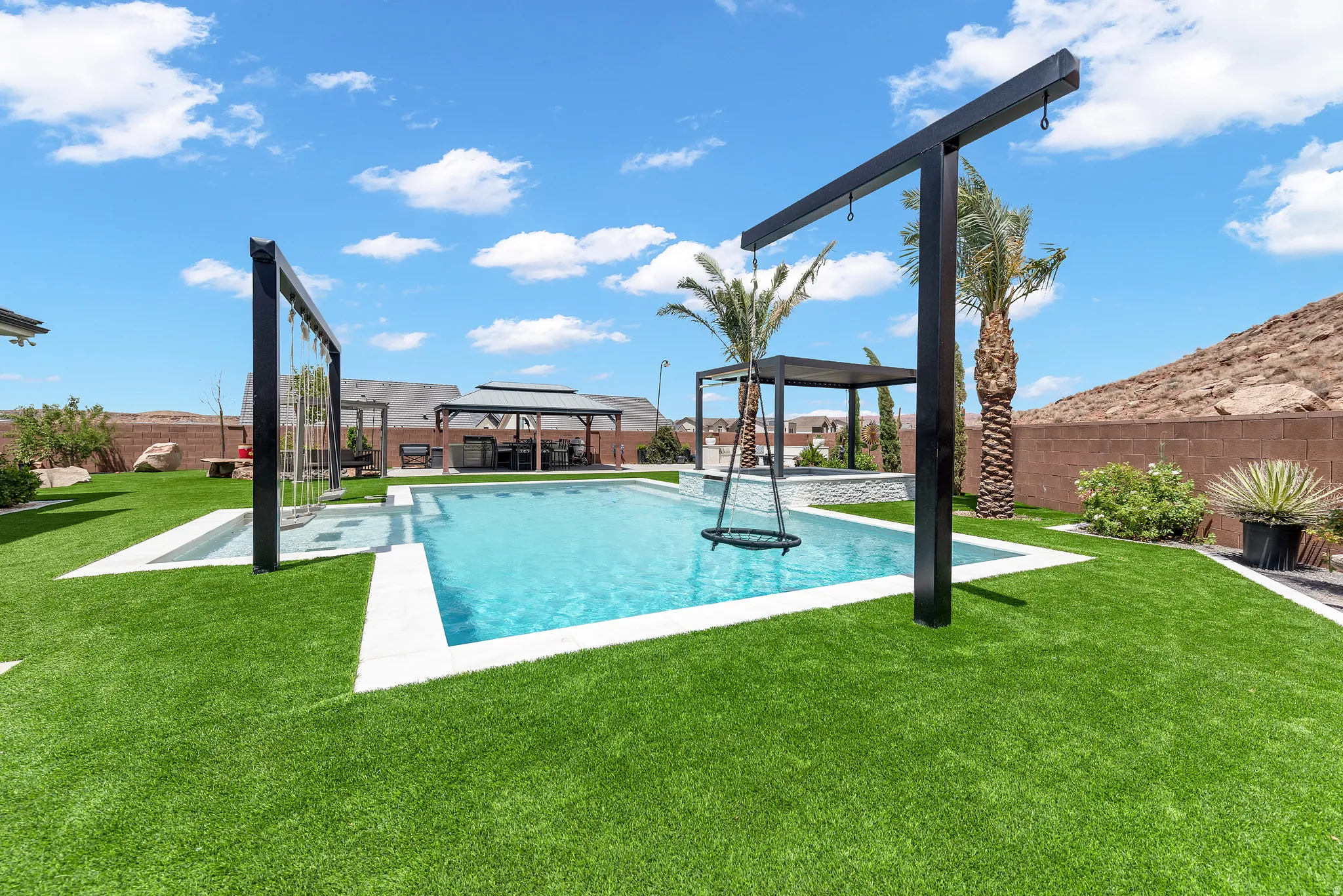 Expansive backyard featuring a rectangular swimming pool with white coping, artificial turf, a built-in pergola structure, mature palm trees, and perimeter fencing