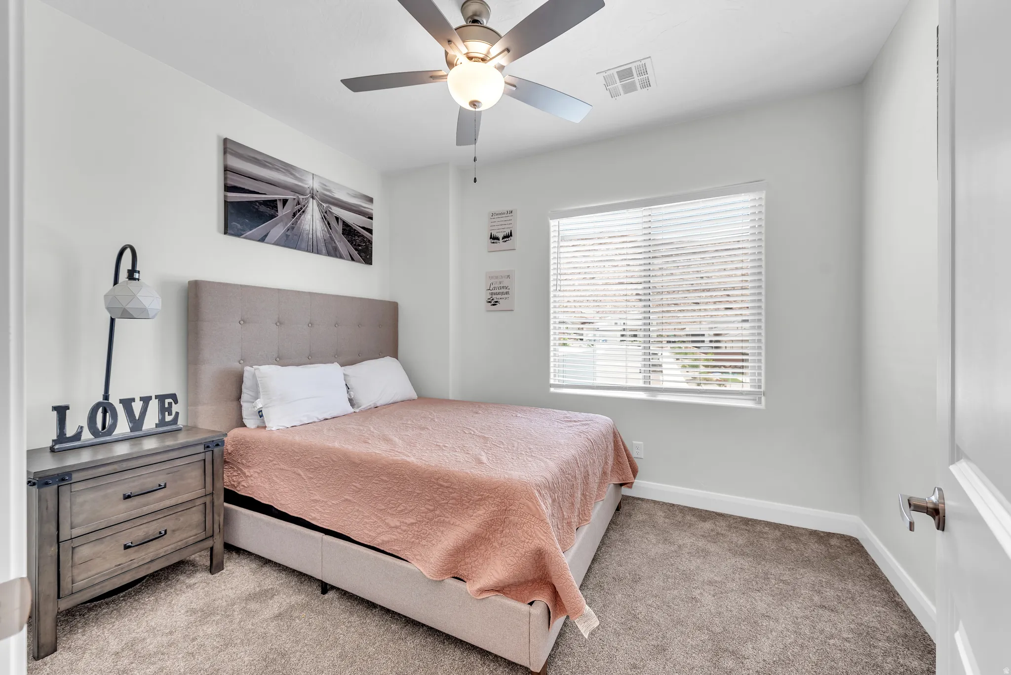 Neutral wall paint, ceiling fan with integrated lighting, window with blinds, light-toned carpet, and a white door with brushed nickel hardware