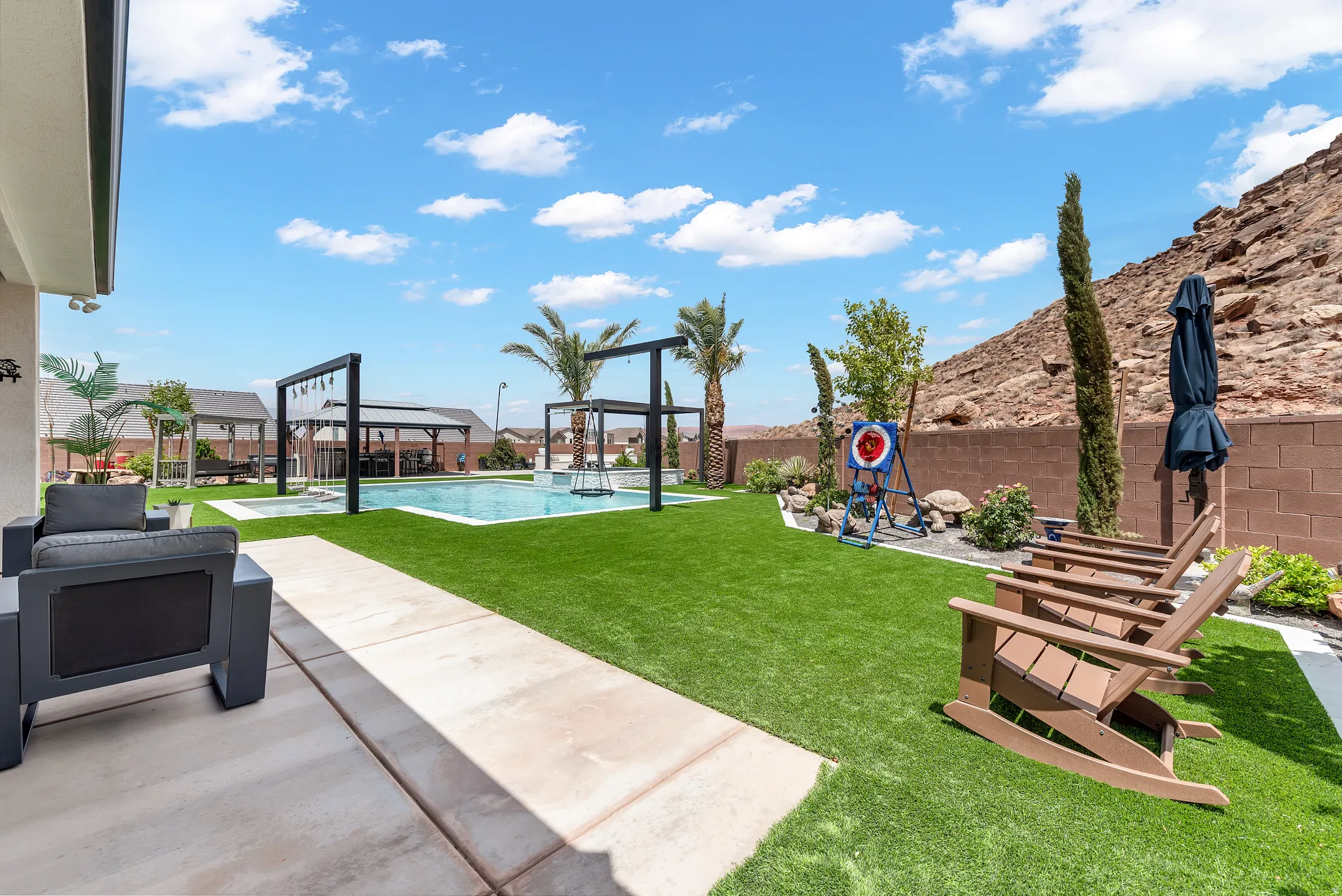 Expansive backyard featuring a central swimming pool with surrounding turf, a concrete patio, and a block wall perimeter