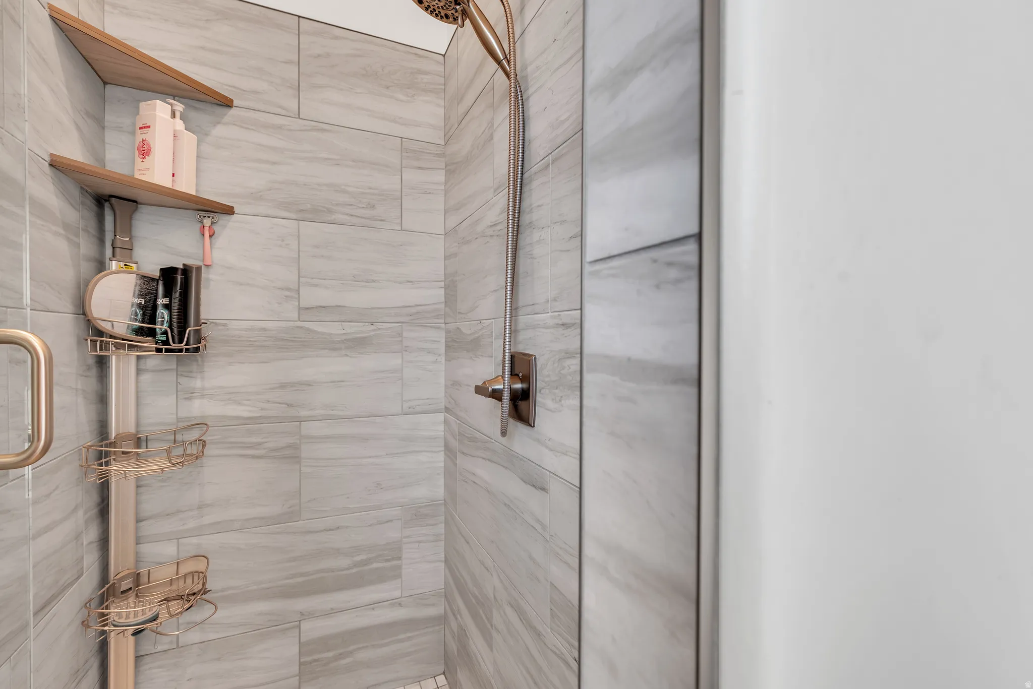 Shower stall featuring large-format tile walls, a rain showerhead, a wall-mounted shower handle, and a glass shower door with a brass handle