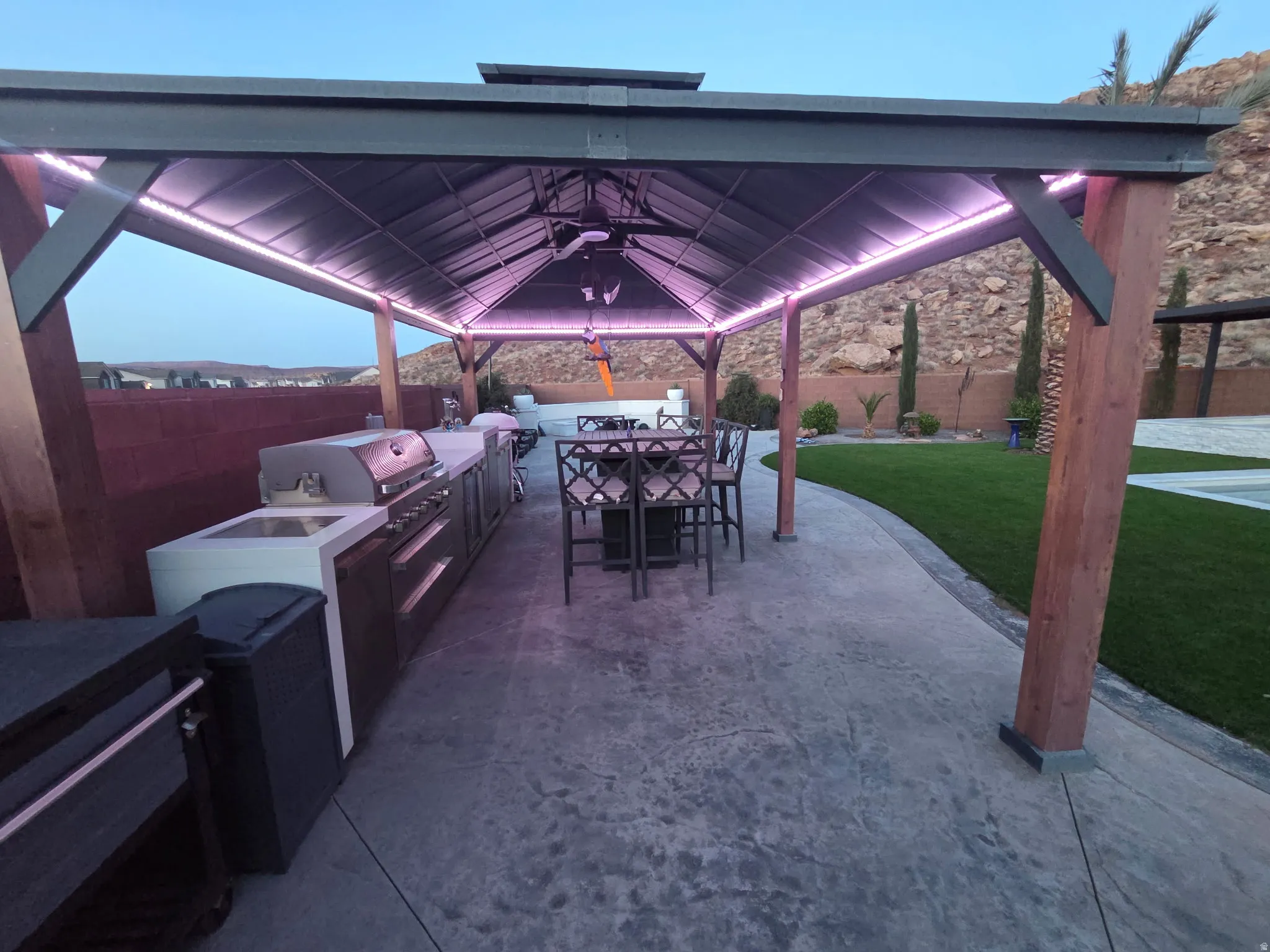 Expansive outdoor living area featuring a covered patio with integrated lighting, a ceiling fan, and substantial wood support pillars